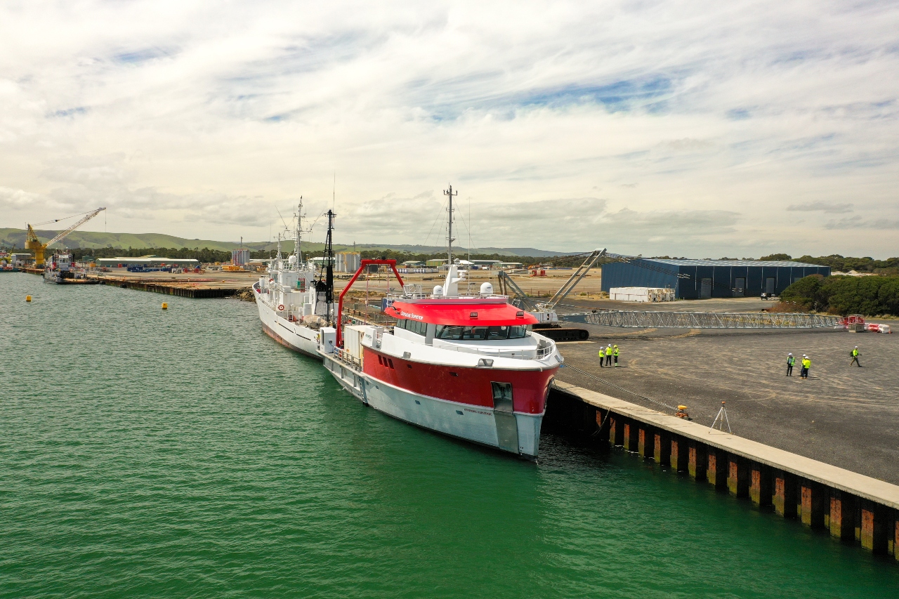 Offshore survey vessel docked at a port with workers onshore