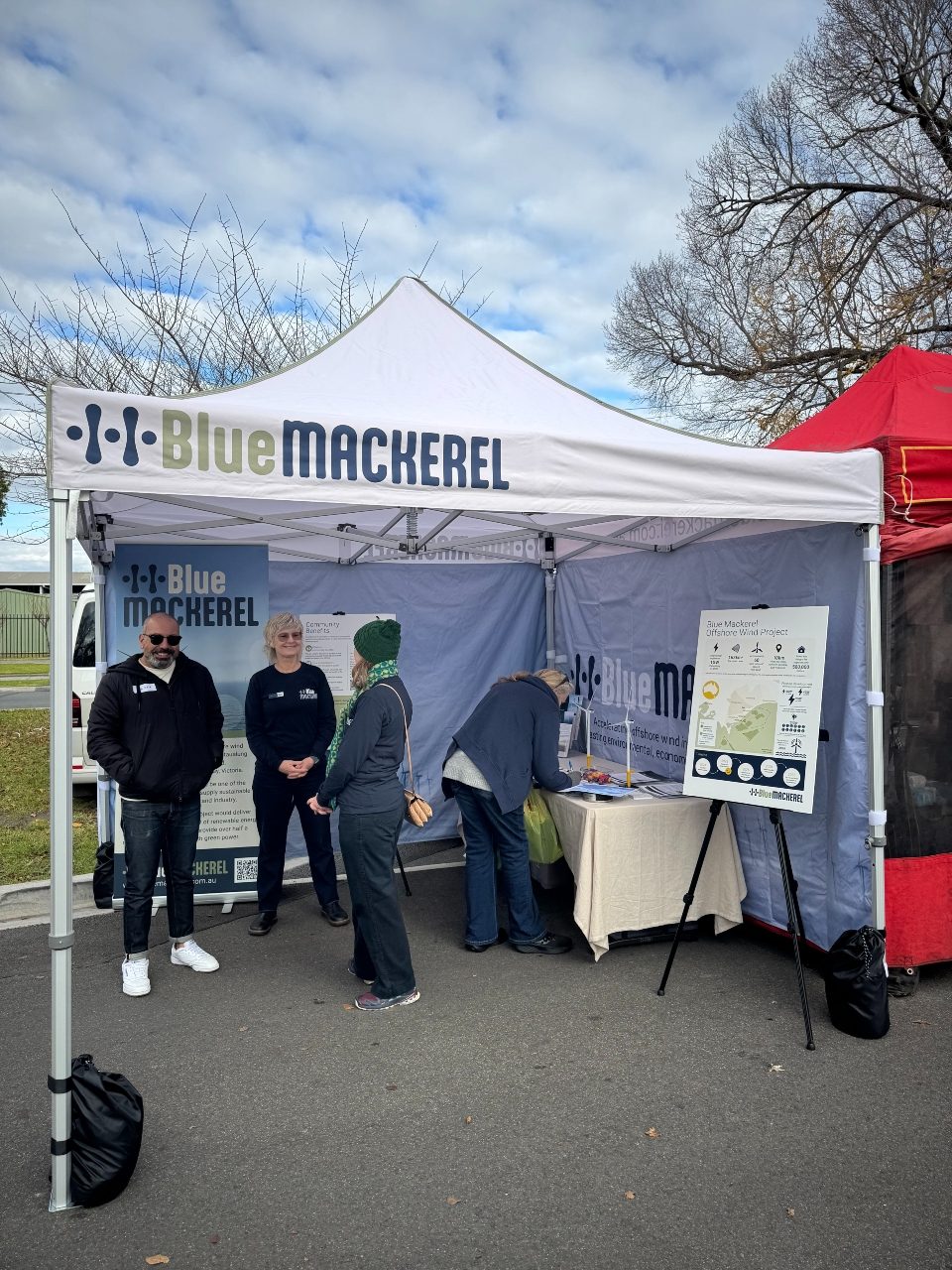 People gathered at a Blue Mackerel information booth under a white canopy outdoors