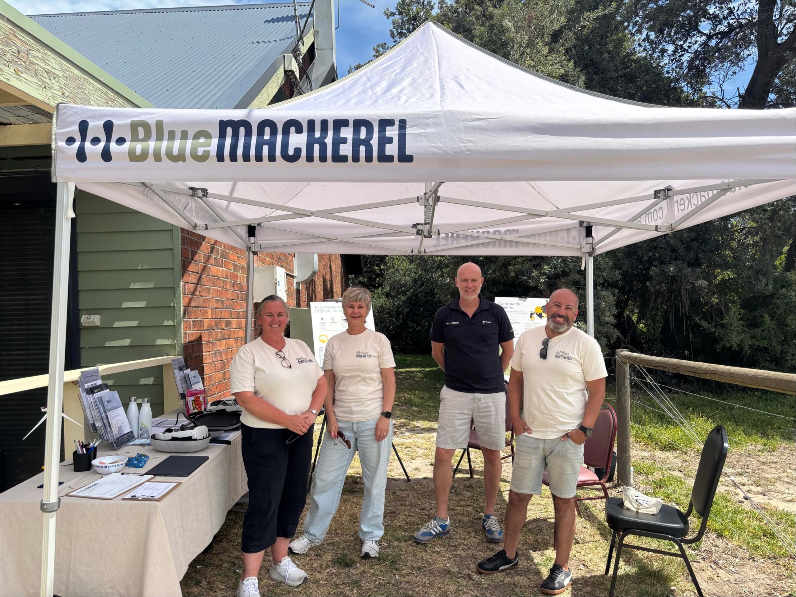 Four people standing under a Blue Mackerel branded white canopy outdoors