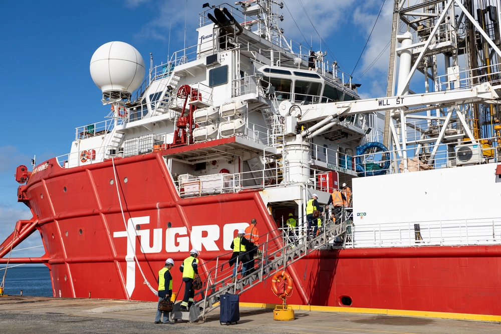 Crew members boarding a large red and white Fugro vessel at dock